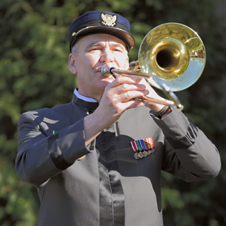 Photo of Scott Shelsta, a middle aged man in a 1890's era military uniform, standing and holding a trombone in playing position.